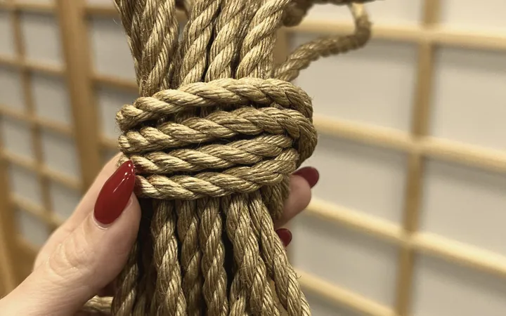 A hand with red nails holds a bundle of jute rope against shoji screens.