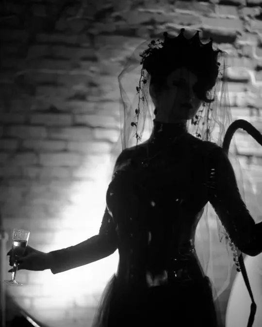 A silhouette in a crown holding a glass against a lit brick wall.