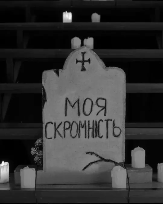 A mock tombstone reading ‘My modesty’, surrounded by candles.