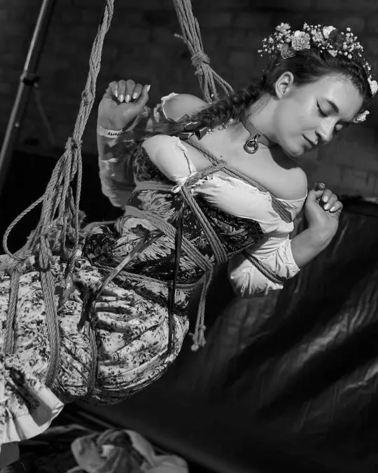 A performer with flowers in her hair rests in a rope suspension.