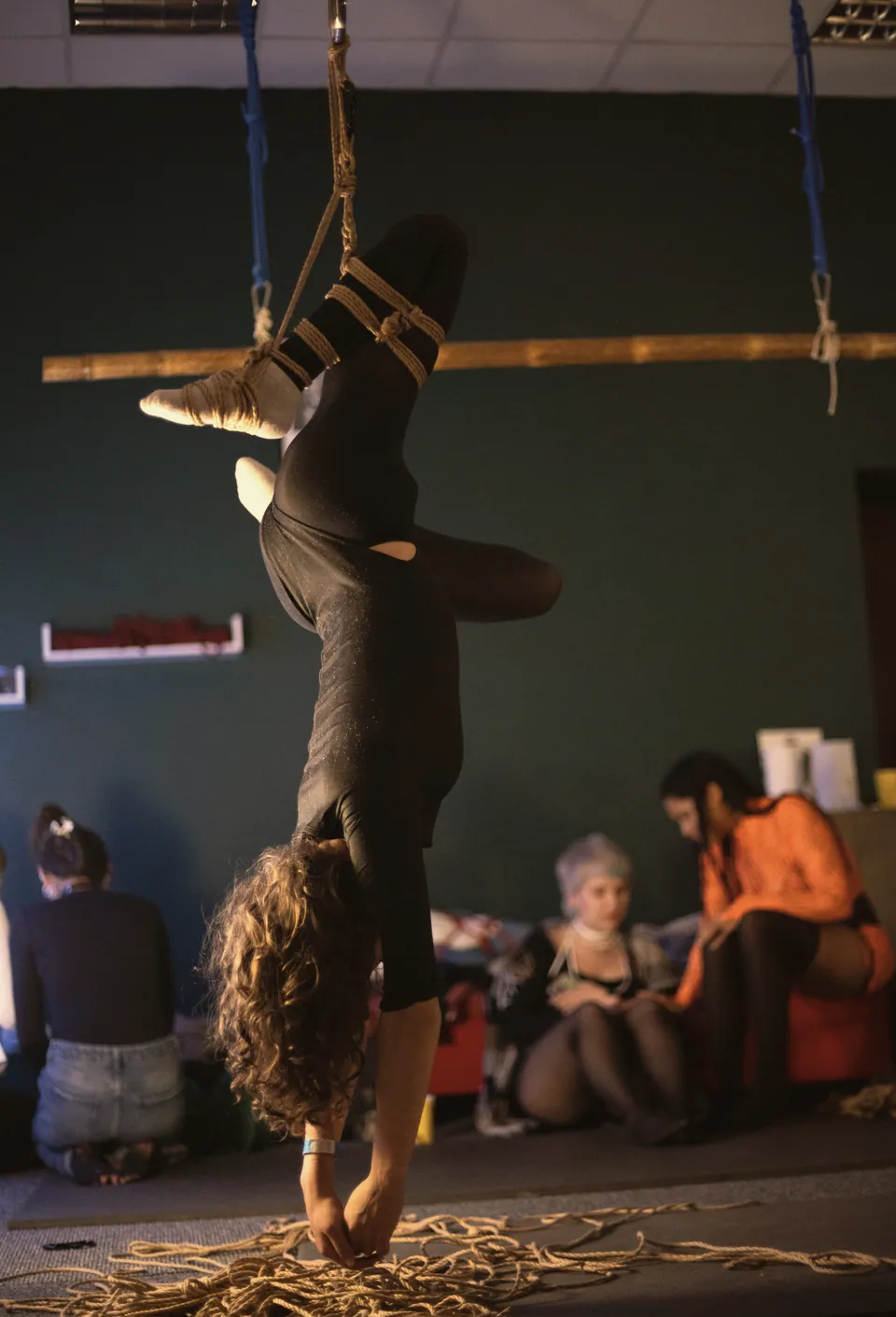 An inverted rope suspension above a floor strewn with jute while guests watch from the floor.